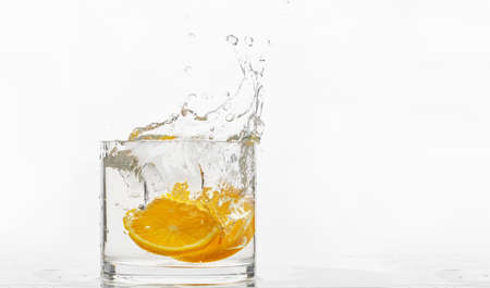 glass container with liquid, fallen orange slices, splash of water on a white backgroundの写真素材