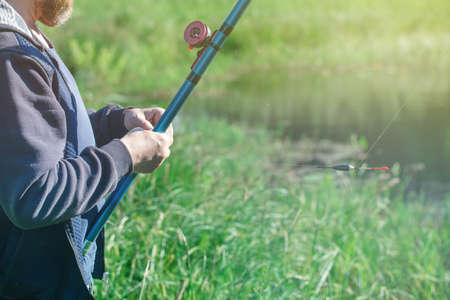 a man with a beard is fishing on a summer day, standing on the bank of a forest pondの写真素材