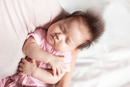a baby girl in the arms of her mother, on a light background of the heelの写真素材