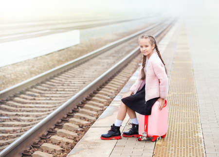 a girl with a pink suitcase is waiting for a train on the station platformの写真素材