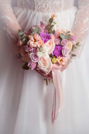 wedding bouquet in the hands of the bride on the background of a white dressの写真素材