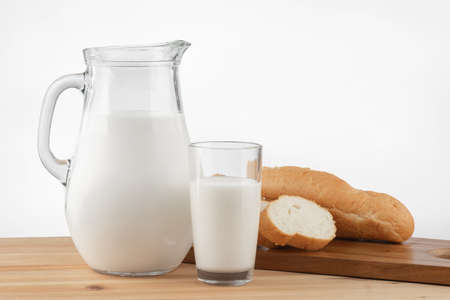 a glass jug with milk and a glass stand on a wooden table with a linen tableclothの写真素材