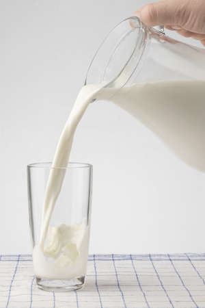 a glass jug with milk and a glass stand on a wooden table with a linen tableclothの写真素材