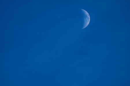 the growing moon in the first quarter with craters on the background of the blue evening sky