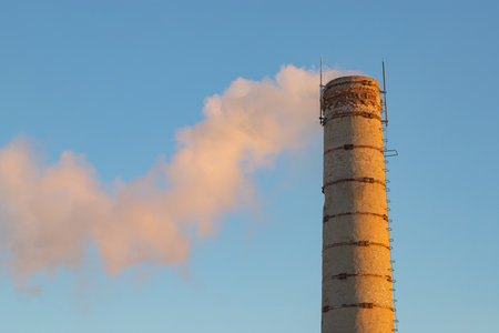 an old brick chimney of a factory boiler room with smoke on a blue sky background, sunny morningの写真素材