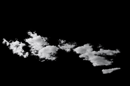 white fluffy clouds standing out against a black background and a blue skyの写真素材