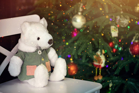 a stuffed toy, a teddy bear in a corduroy jacket, sits on a chair by the Christmas treeの写真素材