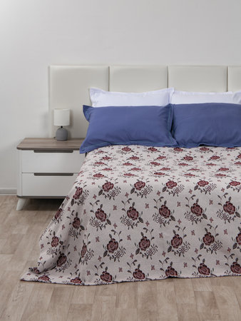A bed with colorful pillows and a jacquard bedspread with a floral pattern, a rug for an armchair