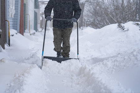 A man in a dark jacket shovels snow near a house, a village street, winter, snowdrifts