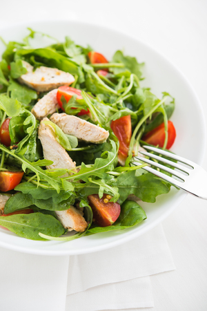 Fresh salad with chicken, tomato and greens (spinach, arugula) on white background close up. Healthy food.の写真素材