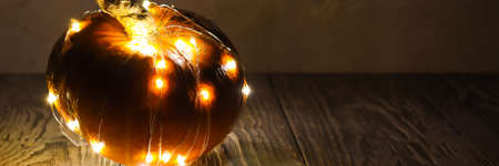 Banner made with a pumpkin wrapped in a festive garland on a wooden table. There is a concrete wall at the back. Front view.の写真素材