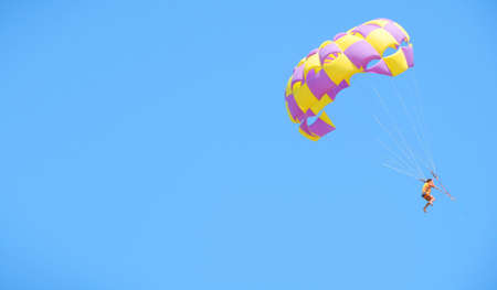 Multicolored parachute against the blue sky. Parasailing in summer. Woman under parachute hanging mid air.  Positive human emotions and feelings  , copy spaceの写真素材