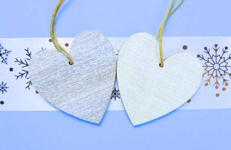 Two wooden hearts placed nicely on a pastel blue with christmas snowflakes background , flat lay,...