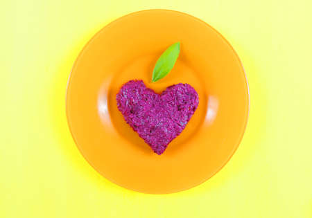 light healthy snacks made from chopped beets, walnuts, garlic and creamy dressing, orange plate background. heart shapeの写真素材