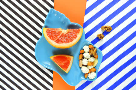 fresh slices red grapefruit and nuts on multicolor background, minimalism, vitamins, healthy diet food conceptの写真素材