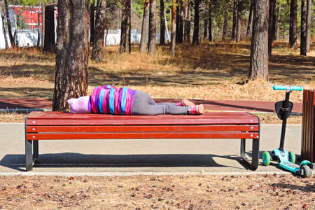 child is resting lying on a bench in the Park tired of riding a scooterの写真素材