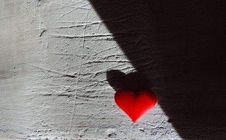 Light and shadow, dramatic effect, red heart and old cement wall with rough deep cracks on stucco surface. Contrast textures of grunge wall and soft fabric heartの写真素材