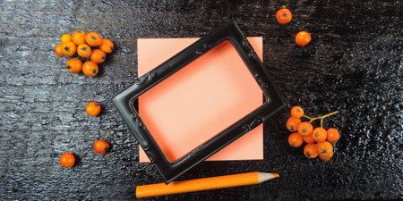 black frame, pink blank stickers and place for text, red berries on a black wooden background