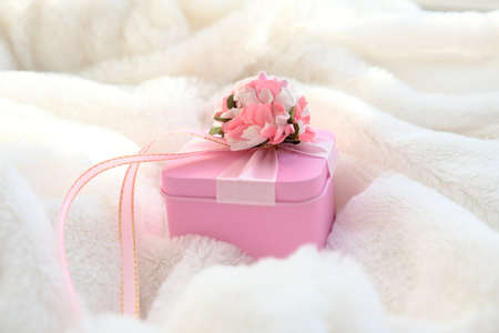 Gift pink box on white fluffy blanket. Details of cozy bedroom, morning for a loved one