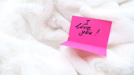 Declaration of love, touching message I love you on pink postcard on  white fluffy blanket. Details...