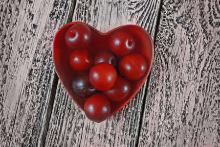 Plum in red plate in  shape  heart on wooden plank background .  Very light diet healthy  breakfast conceptの写真素材