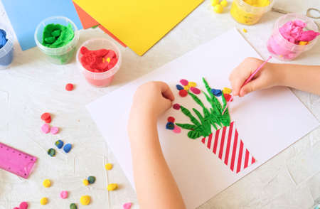 Child making homemade greeting card. little girl making vase with flowers from paper and clay,...