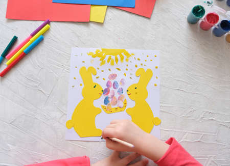 Child making card with Easter bunnies from colorful paper. Applique. Handmade. Project of children's creativity, handicrafts, crafts for kids.の写真素材