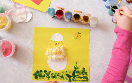 Child making card with Easter chick from colorful paper and cotton pad. Handmade. A project of...