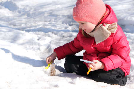 Little girl in warm winter clothes with notepad and pen in her hand investigate details of nature and experimenting with dry plants snow and laboratory flask. Winter outdoor kids activity learningの写真素材