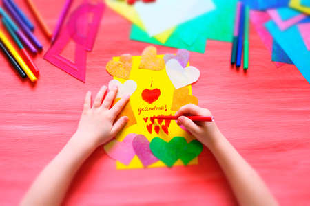 Little girl making card for grandma. Colorful pink background with paper decoration, multicolored hearts,  Handmade concept for birthday, mothers day and grandparents dayの写真素材