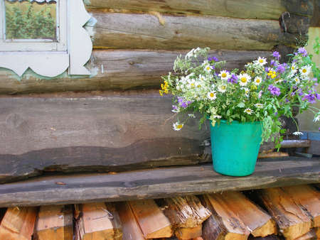 Still life in a rustic style. Old wooden hut, a log house, a large bouquet of wild flowers in an old bucket. Granny's cozy home. Authentic houseの写真素材