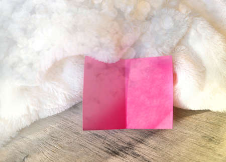 Soft focus of pink note card on white folds fur background, close-up. Cozy, soft, minimal. Love and...
