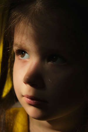 Dramatic portrait of sad little child girl with tear on the cheek and shadow on face. lonely in dark. Childhood and problems of parents and children concept.の写真素材