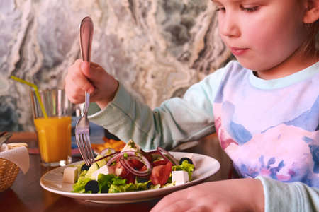Child eating greek salad in cafeの写真素材
