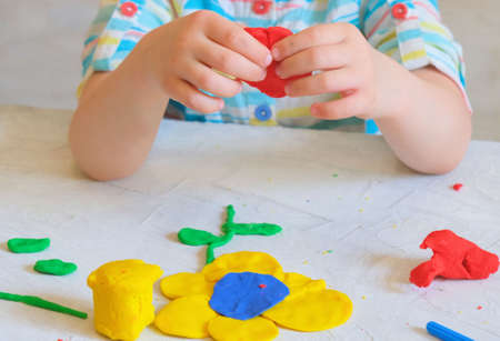 Hands of little girl making flower from colorful clay dough, plasticine, Home Education game with clay. Early development concept. Educational and entertaining classes with childrenの写真素材