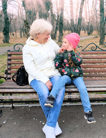 Grandmother with her granddaughter hugging and talking sitting on a bench in the parkの写真素材