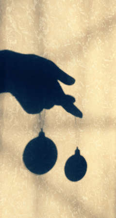 Blurred view shadow on beige wall with neutral pattern female hand and christmas toys balls,...