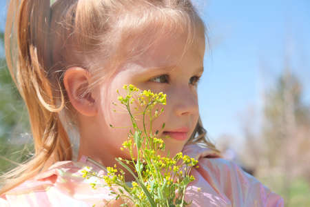 Portrait of little girl with spring wildflowers outdoors. Kids being kids concept. Authentic photo...