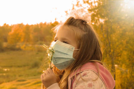 preschool girl in Medical blue disposable protective mask at the evening for a walk at sunsetの写真素材
