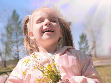 Portrait of little girl with spring wildflowers outdoors. Kids being kids concept. Authentic photo of child. Spring vibes. Haze filterの写真素材