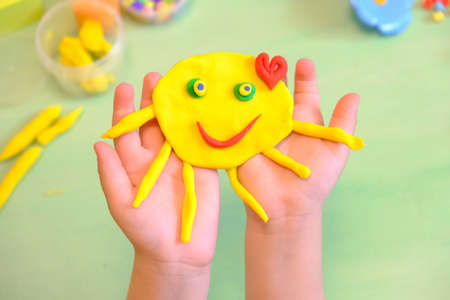 Child playing with plasticine, colorful modeling clay and sculpting funny sun. Home Education game with clay. Early development. Handmade concept for birthday, mothers day or valentines dayの写真素材