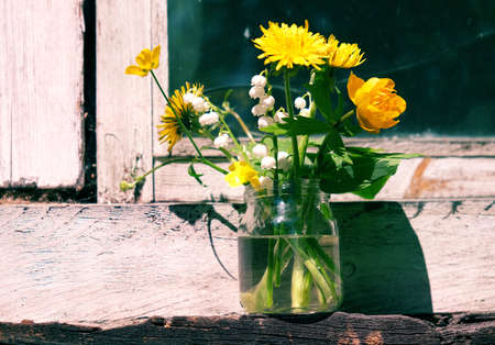 Summer flowers in glass jar on old windowsill in sunlightの写真素材