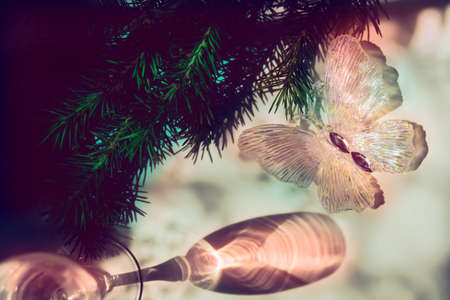 Blurred shadow of wine glass with light passes through glass.  branch of Christmas tree and christmas butterfly toy . Abstract, play of light and shadow, shadow play illusion . Christmas still lifeの写真素材