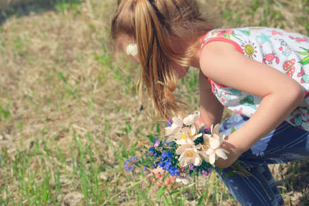 Little girl picking summer flowers in a field. Happy child enjoying nature outdoorsの写真素材