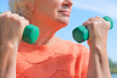 Senior woman doing physical exercise outdoors with dumbbells.  Senior healthcare and sport concept.の写真素材