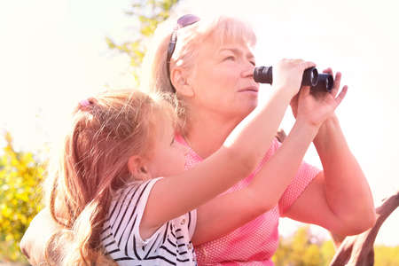 Little girl with her grandmother looking through binoculars outdoorの写真素材