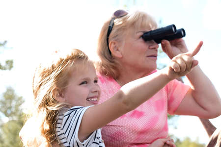 Little girl with her grandmother looking through binoculars outdoorの写真素材