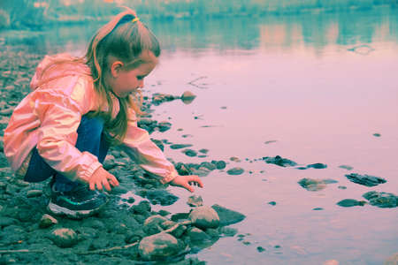 Child girl standing on stones rock in natural stream in springtime or autumn and playing with stones. investigate details of nature. outdoor kids activity and learning conceptの写真素材