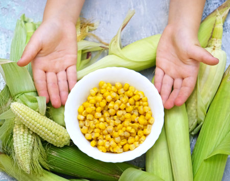 Plate with corn in child`s hand, cob of corn on the tableの写真素材