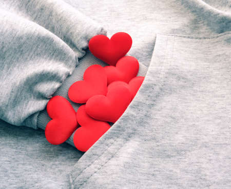 Textile gray melange woolen clothes and many red hearts inside pocket. Concept of love and kindness...